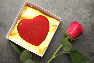 Photo of Heart shaped chocolate in box and red rose on grey table, flat lay