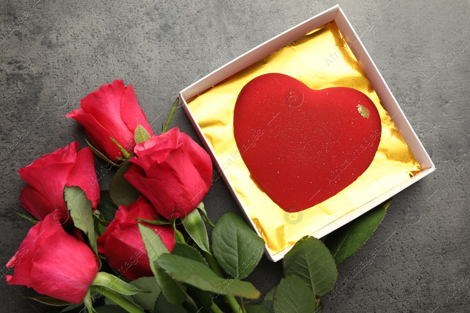 Photo of Heart shaped chocolate in box and red roses on grey table, flat lay