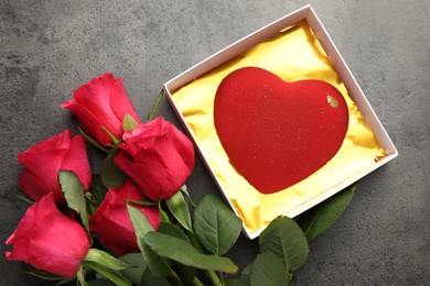 Photo of Heart shaped chocolate in box and red roses on grey table, flat lay