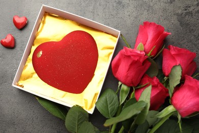 Photo of Heart shaped chocolate in box, decorative hearts and red roses on grey table, flat lay