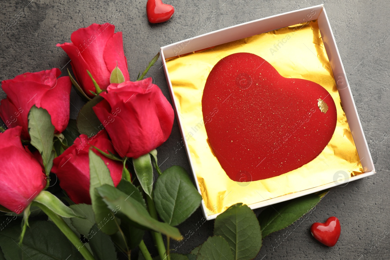 Photo of Heart shaped chocolate in box, decorative hearts and red roses on grey table, flat lay