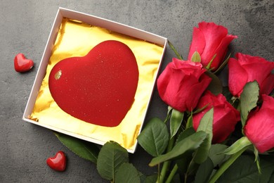 Photo of Heart shaped chocolate in box, decorative hearts and red roses on grey table, flat lay