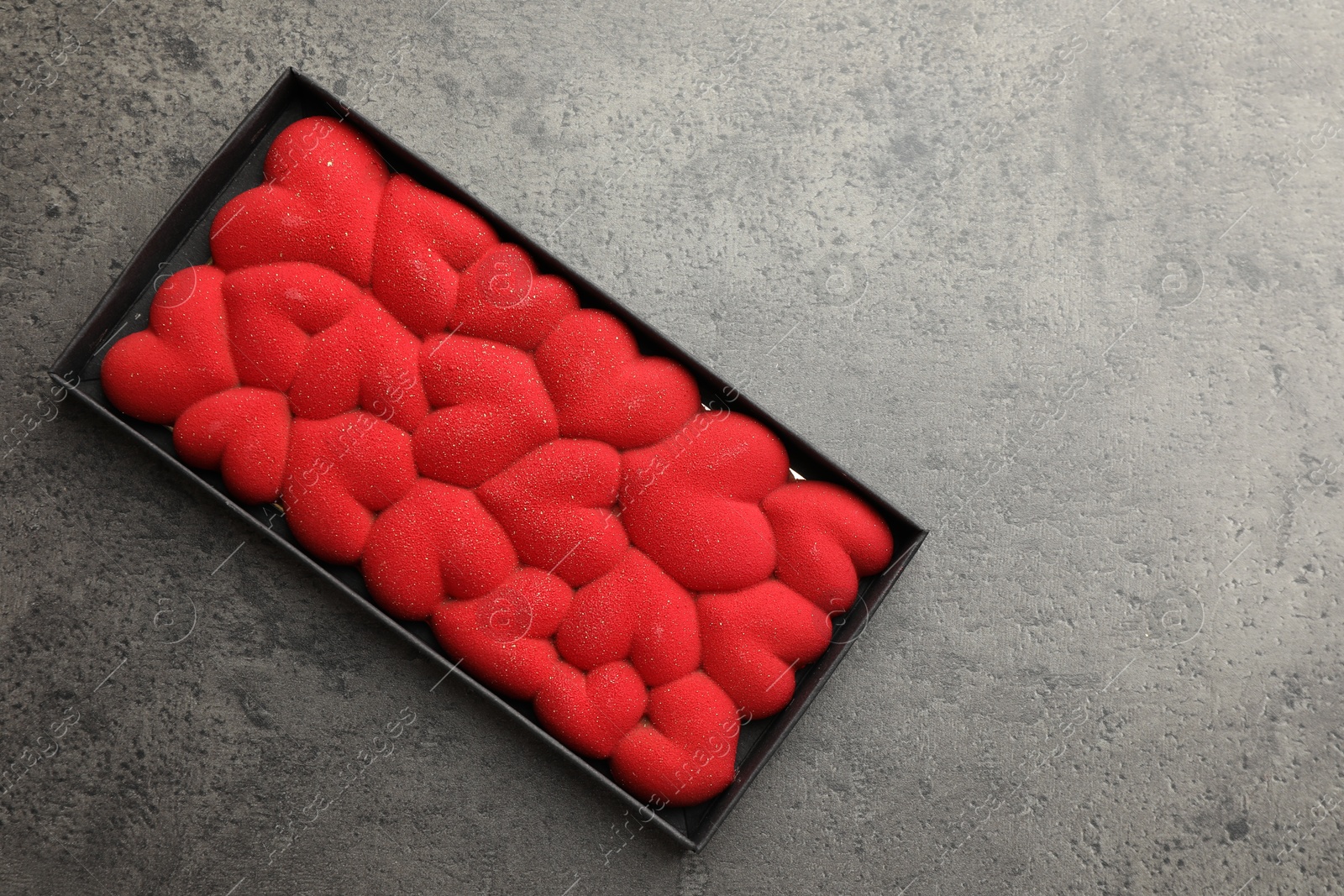 Photo of Chocolate bar decorated with hearts in box on grey table, top view. Space for text