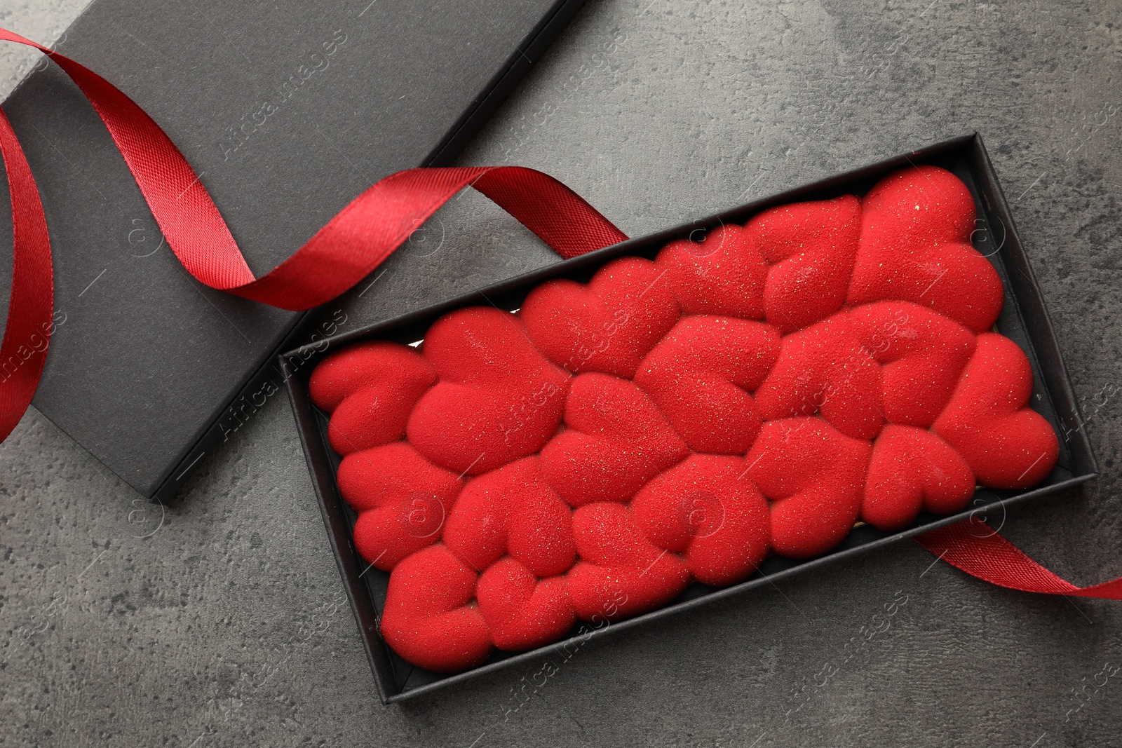 Photo of Chocolate bar decorated with hearts in box and red ribbon on grey table, flat lay