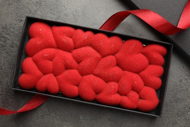 Photo of Chocolate bar decorated with hearts in box and red ribbon on grey table, flat lay