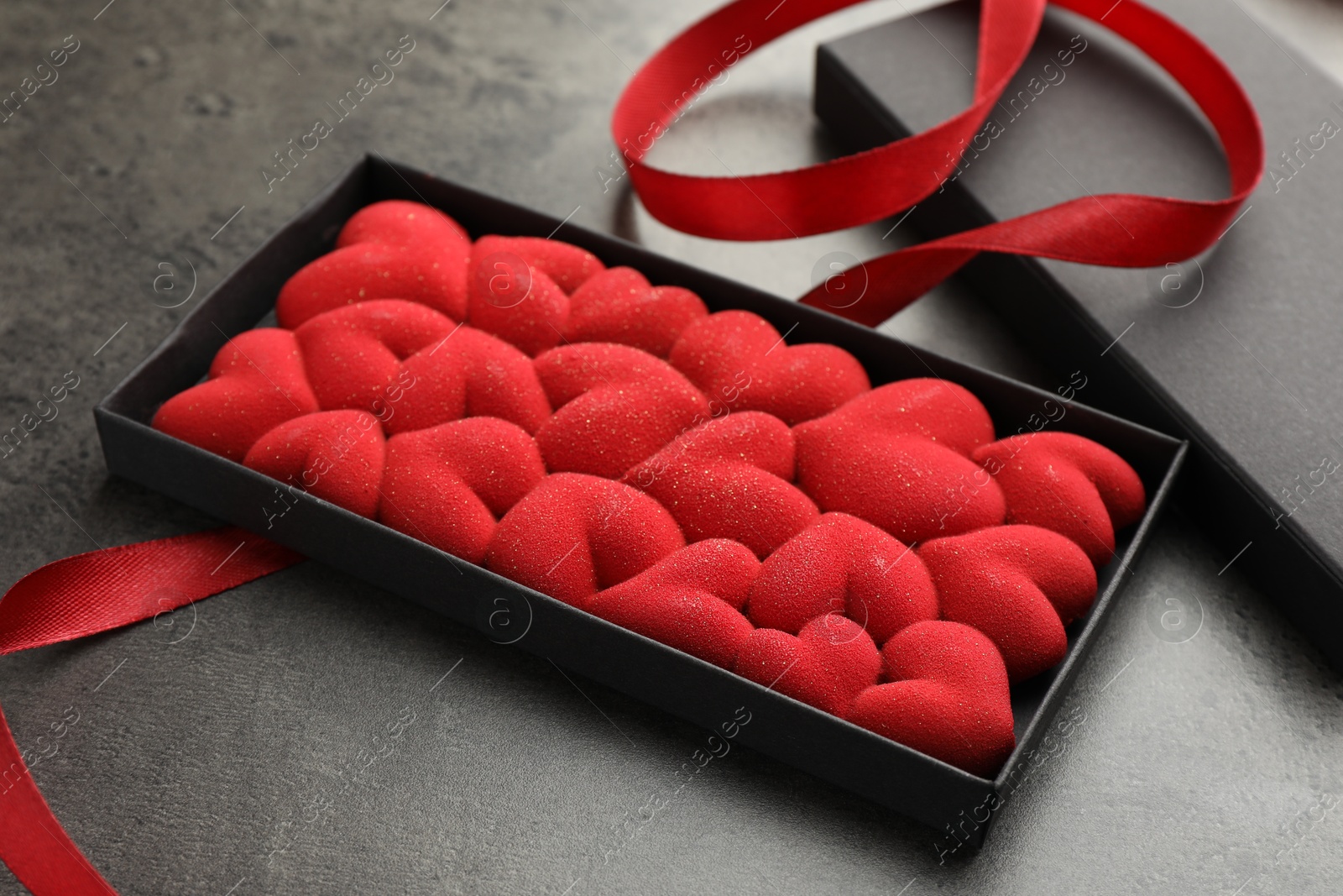 Photo of Chocolate bar decorated with hearts in box and red ribbon on grey table, closeup