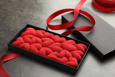 Photo of Chocolate bar decorated with hearts in box and red ribbon on grey table, closeup