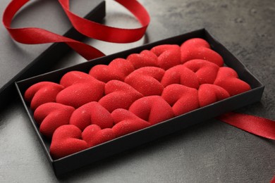 Photo of Chocolate bar decorated with hearts in box and red ribbon on grey table, closeup