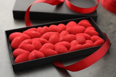 Photo of Chocolate bar decorated with hearts in box and red ribbon on grey table, closeup