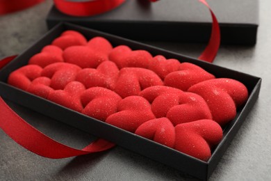 Photo of Chocolate bar decorated with hearts in box and red ribbon on grey table, closeup