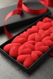 Photo of Chocolate bar decorated with hearts in box and red ribbon on grey table, closeup