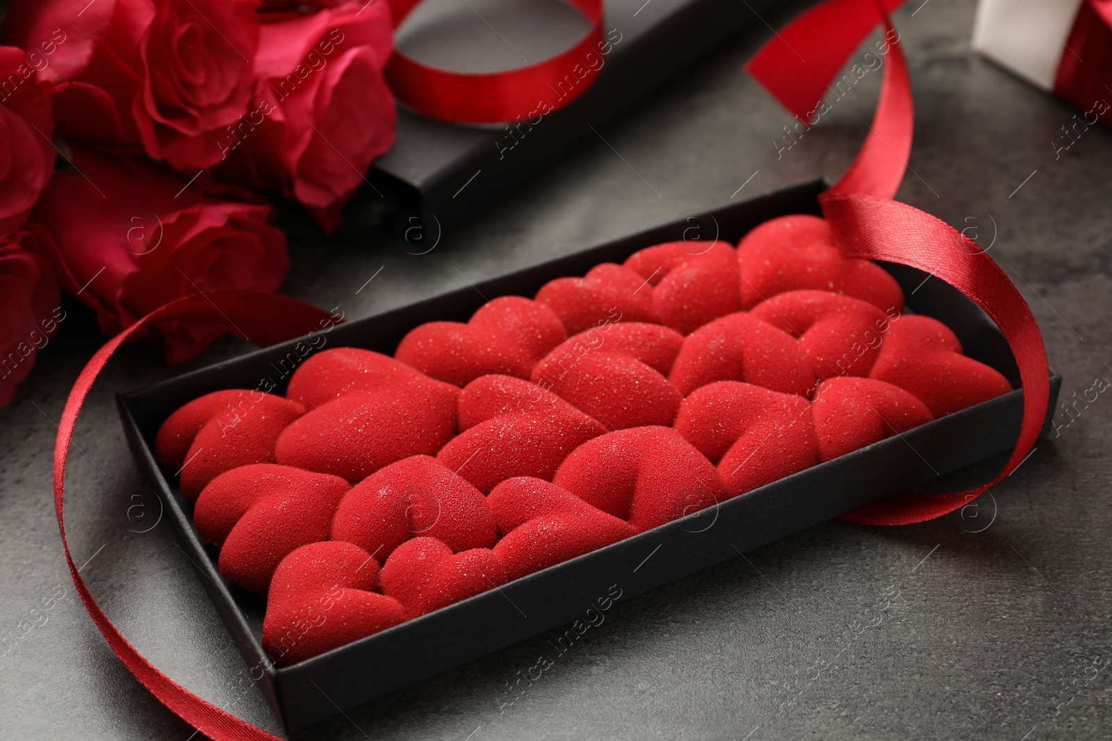 Photo of Chocolate bar decorated with hearts in box, roses and red ribbon on grey table, closeup