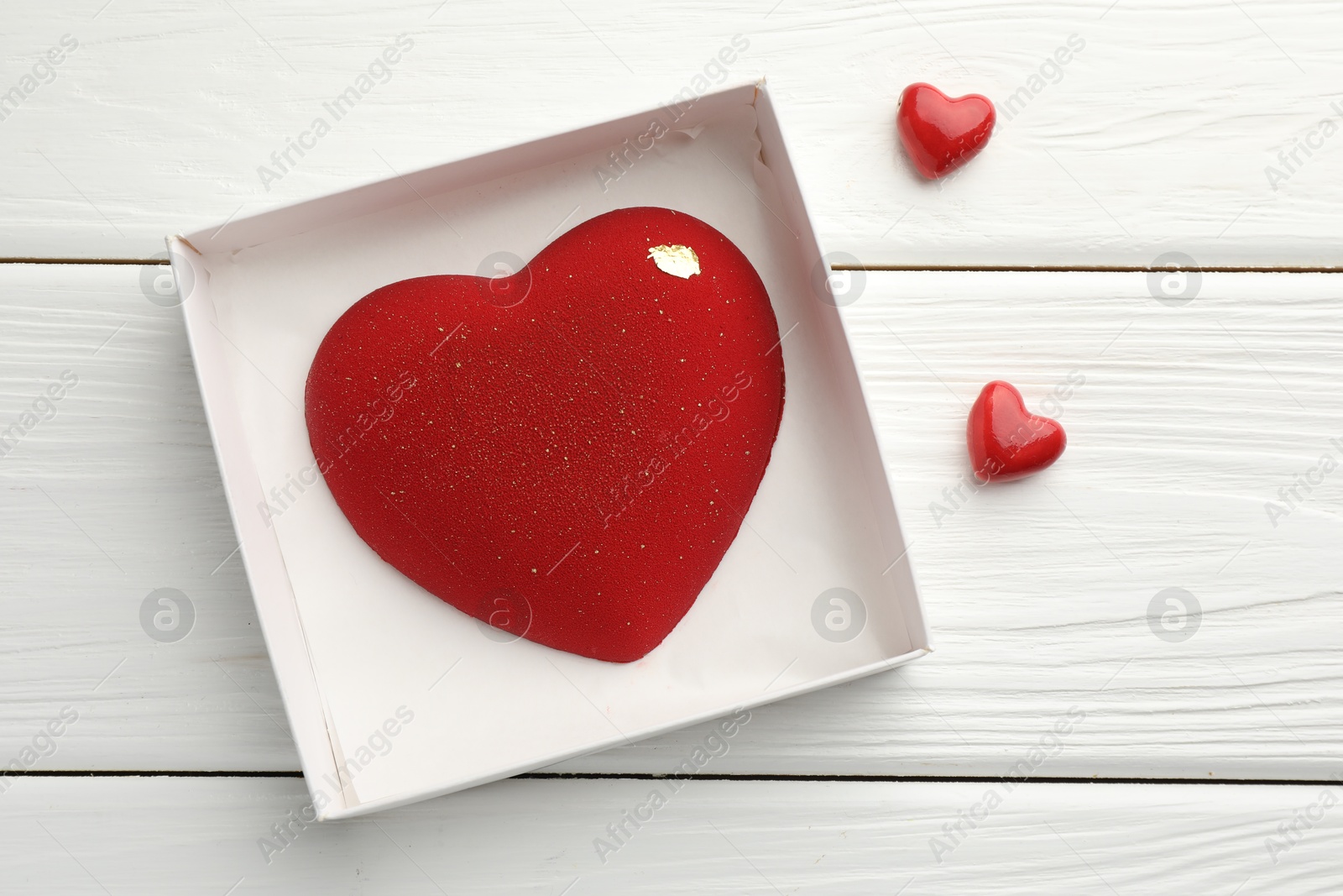 Photo of Heart shaped chocolate in box and decorative hearts on white wooden table, flat lay