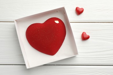 Photo of Heart shaped chocolate in box and decorative hearts on white wooden table, flat lay