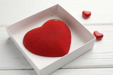 Photo of Heart shaped chocolate in box and decorative hearts on white wooden table, closeup