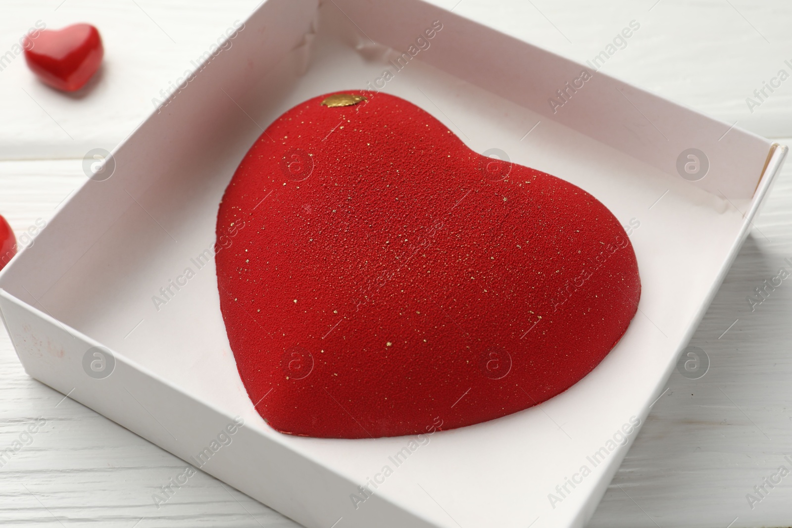 Photo of Heart shaped chocolate in box on white wooden table, closeup