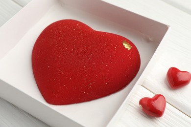 Photo of Heart shaped chocolate in box and decorative hearts on white wooden table, closeup