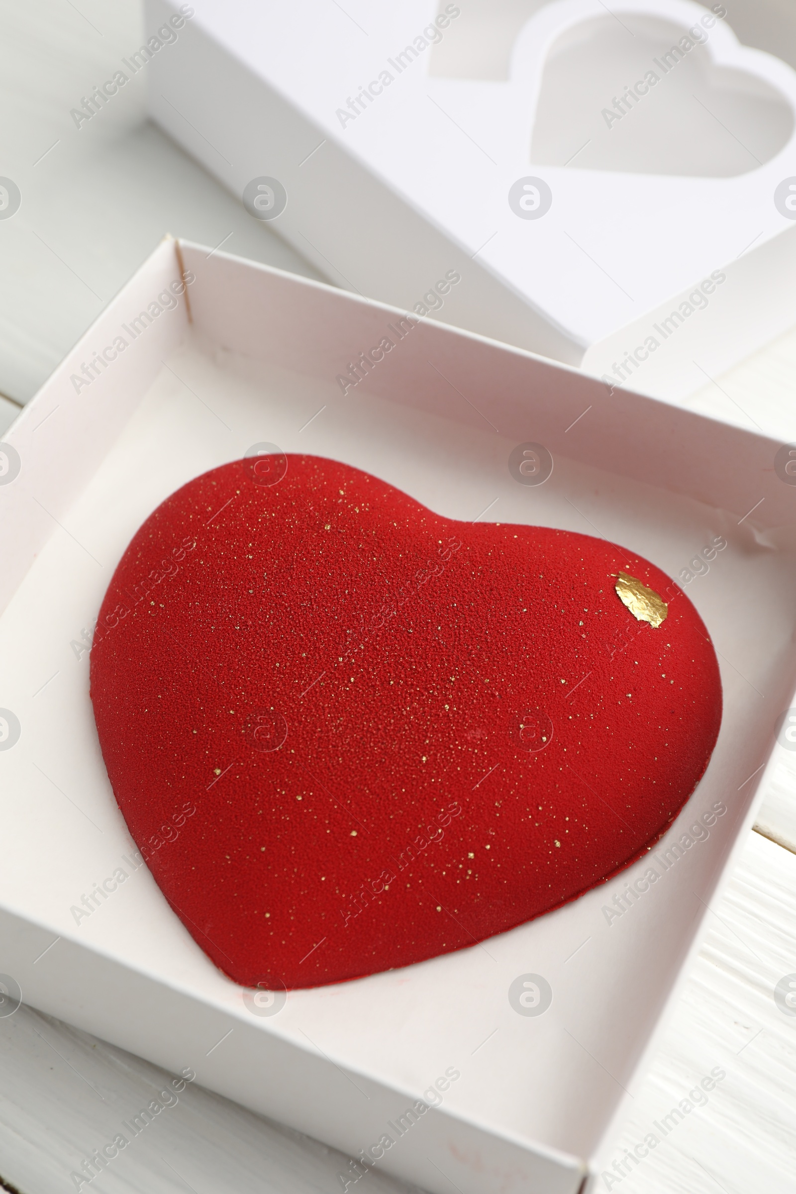 Photo of Heart shaped chocolate in box on white wooden table, closeup