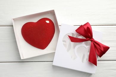 Photo of Heart shaped chocolate in box on white wooden table, flat lay