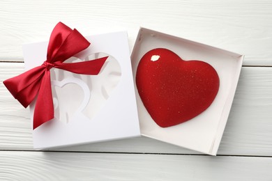 Photo of Heart shaped chocolate in box on white wooden table, flat lay