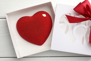 Photo of Heart shaped chocolate in box on white wooden table, flat lay