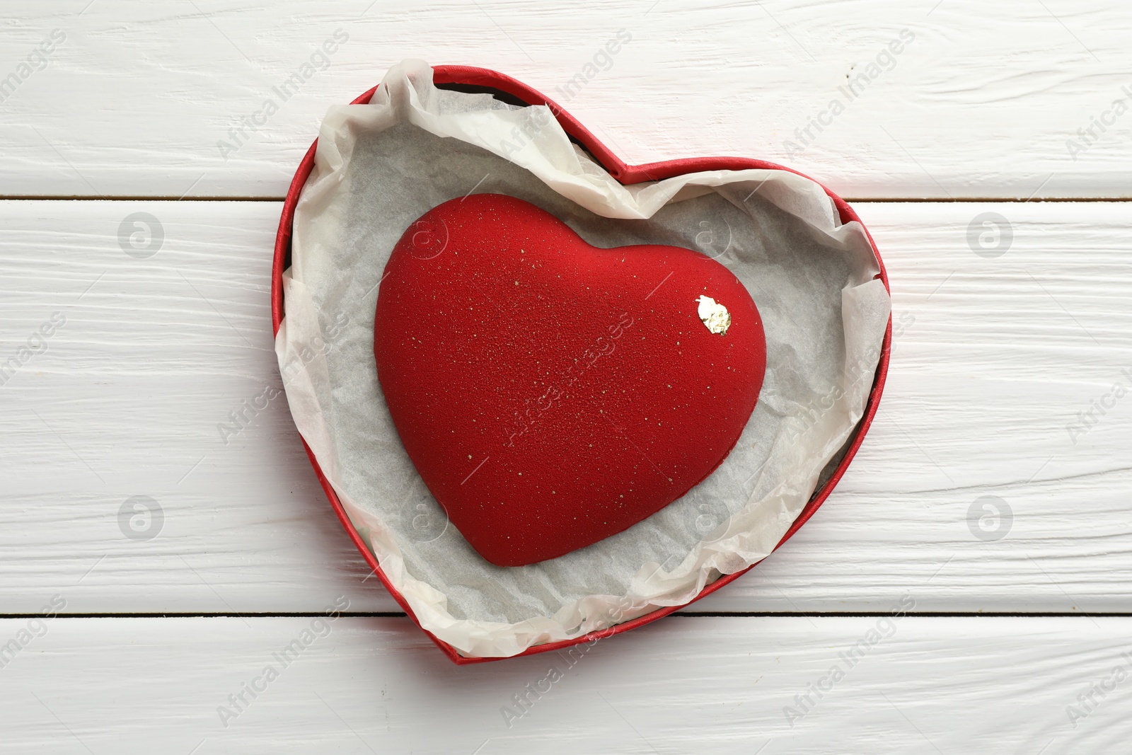 Photo of Heart shaped chocolate in box on white wooden table, top view