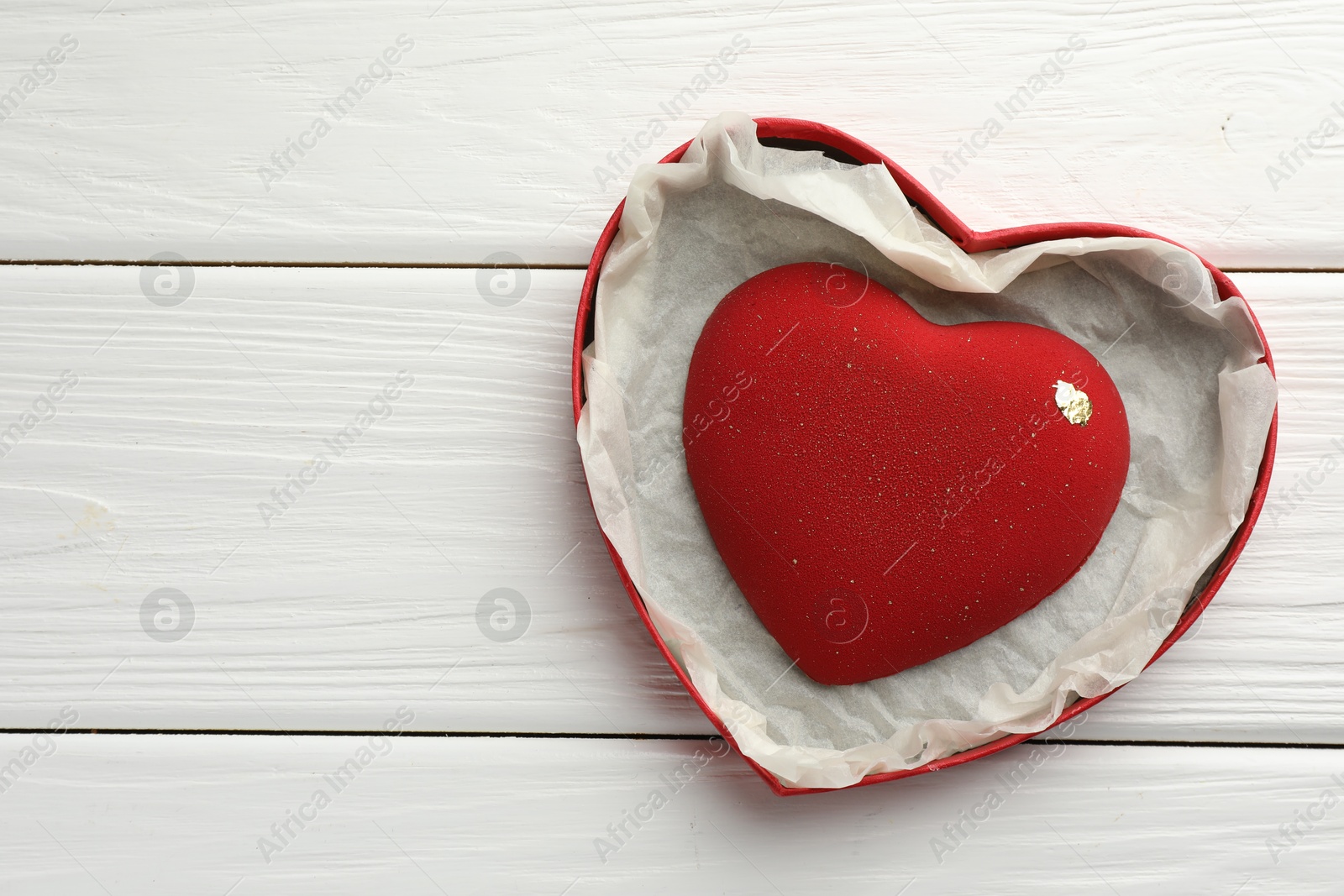 Photo of Heart shaped chocolate in box on white wooden table, top view. Space for text