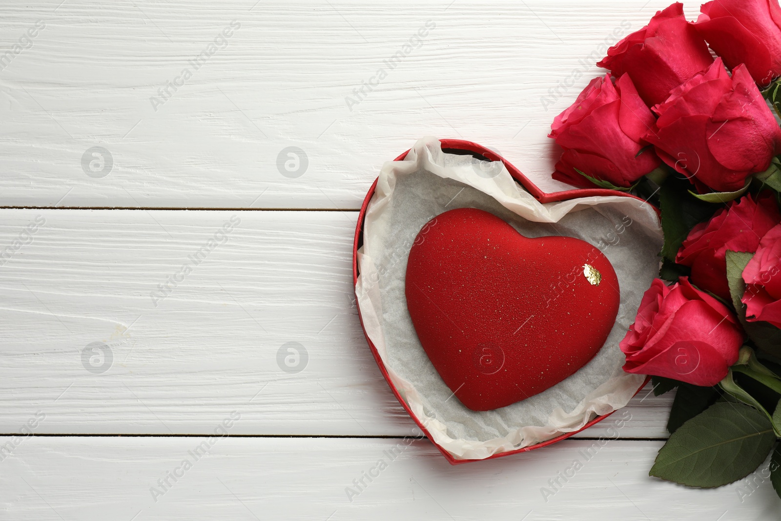 Photo of Heart shaped chocolate in box and red roses on white wooden table, flat lay. Space for text