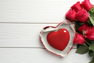 Photo of Heart shaped chocolate in box and red roses on white wooden table, flat lay. Space for text