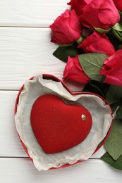 Photo of Heart shaped chocolate in box and red roses on white wooden table, flat lay