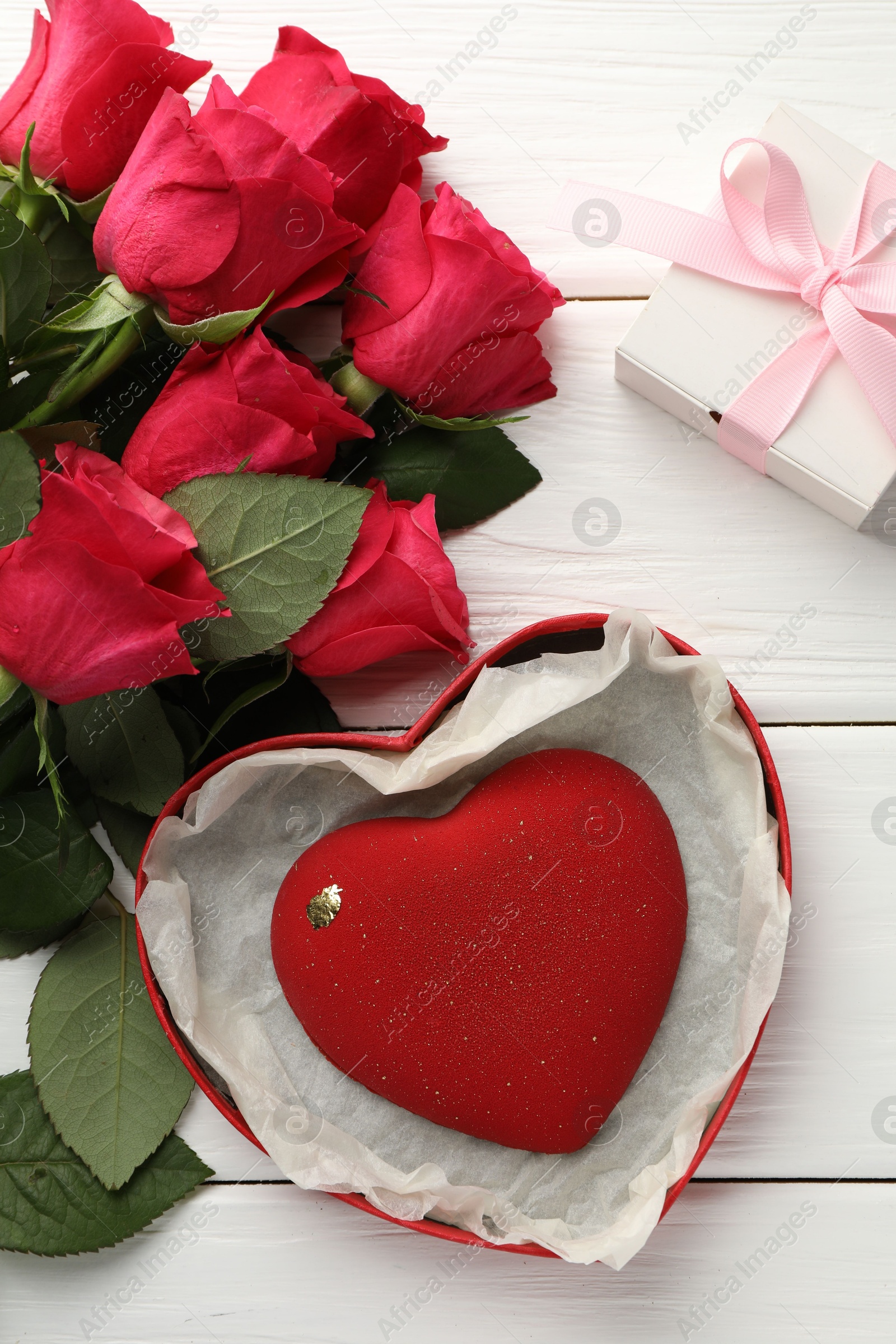 Photo of Heart shaped chocolate in box and red roses on white wooden table, flat lay