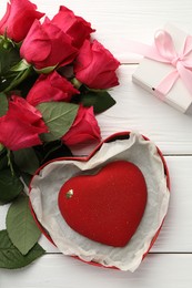 Photo of Heart shaped chocolate in box and red roses on white wooden table, flat lay