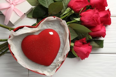 Photo of Heart shaped chocolate in box and red roses on white wooden table, flat lay