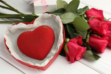 Photo of Heart shaped chocolate in box and red roses on white wooden table, closeup