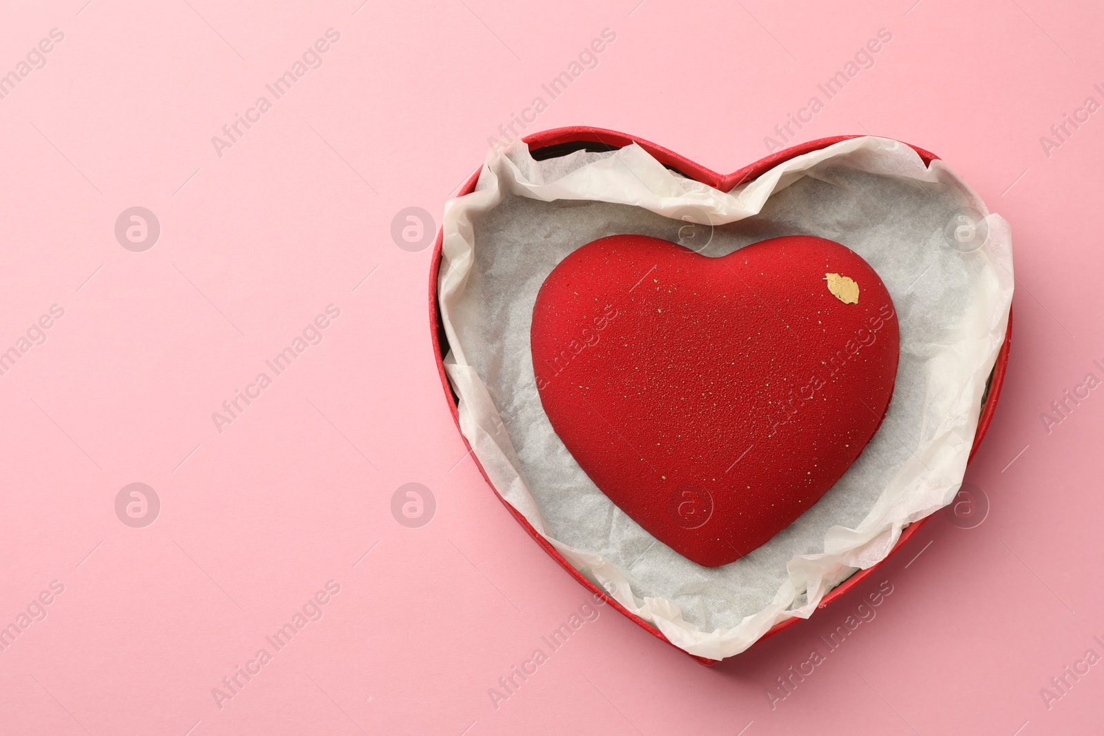 Photo of Heart shaped chocolate in box on pink background, top view. Space for text