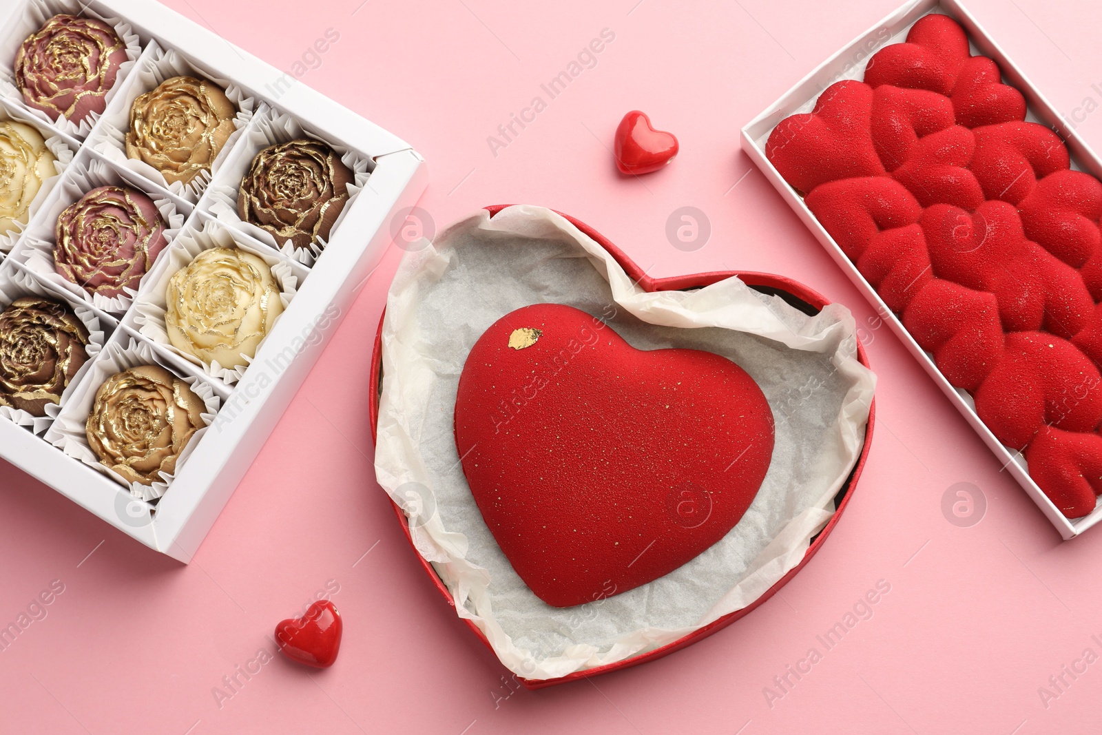 Photo of Heart shaped chocolate and other candies on pink background, flat lay