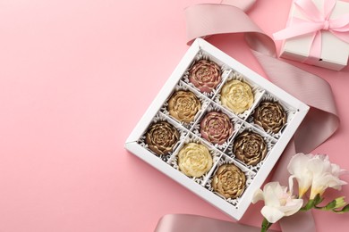 Photo of Flower shaped chocolate bonbons in box, gift, flowers and ribbon on pink background, flat lay. Space for text