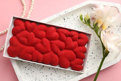 Photo of Chocolate bar decorated with hearts in box, flowers and pearl jewelry on pink background, flat lay