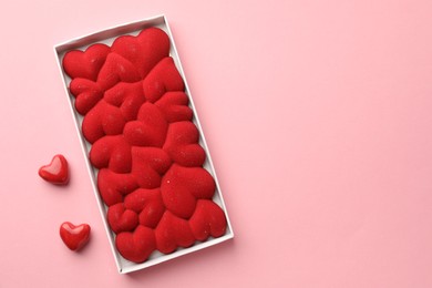 Photo of Chocolate bar decorated with hearts in box on pink background, flat lay. Space for text