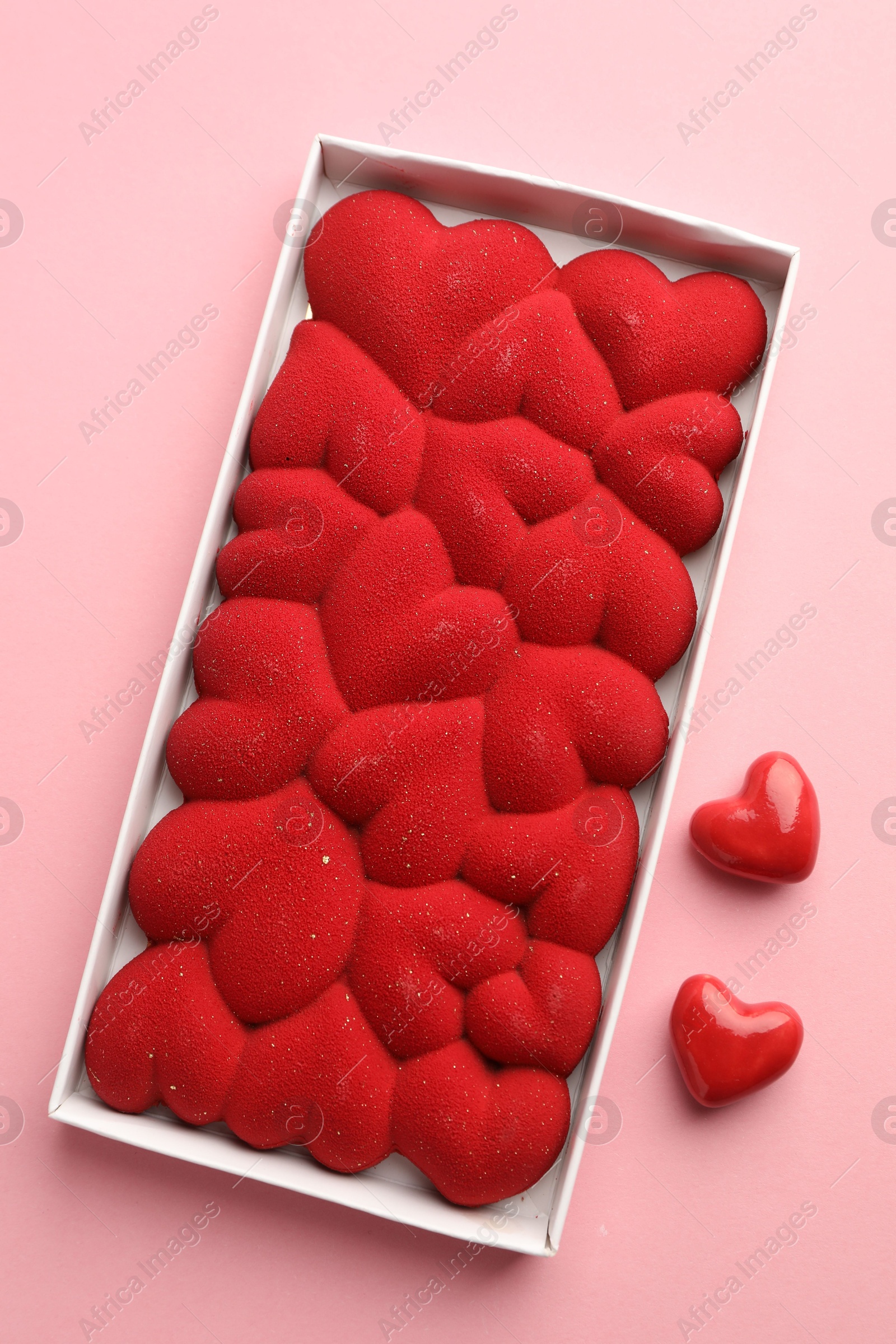 Photo of Chocolate bar decorated with hearts in box on pink background, flat lay