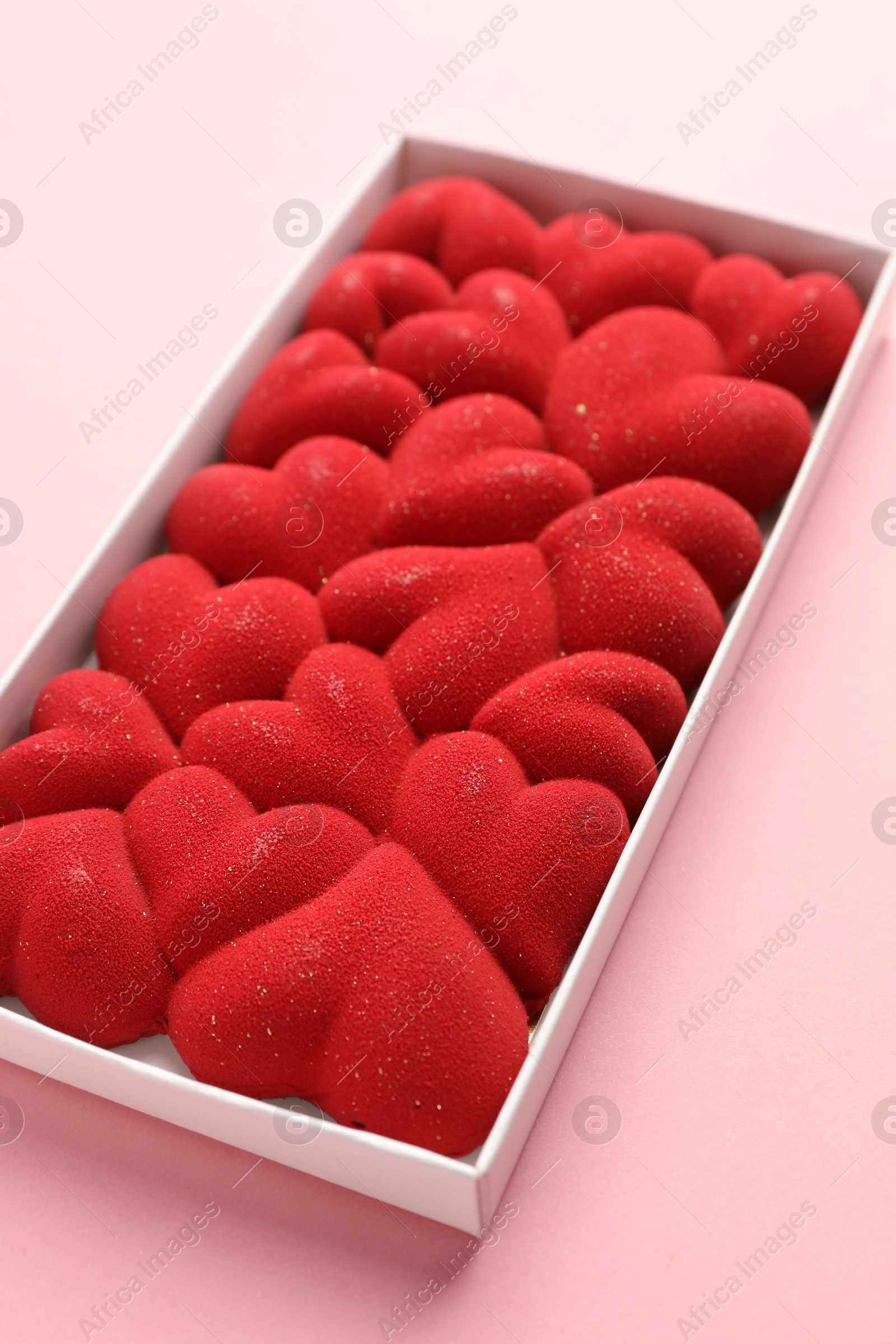 Photo of Chocolate bar decorated with hearts in box on pink background, closeup