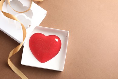 Photo of Heart shaped chocolate in box on brown background, top view. Space for text