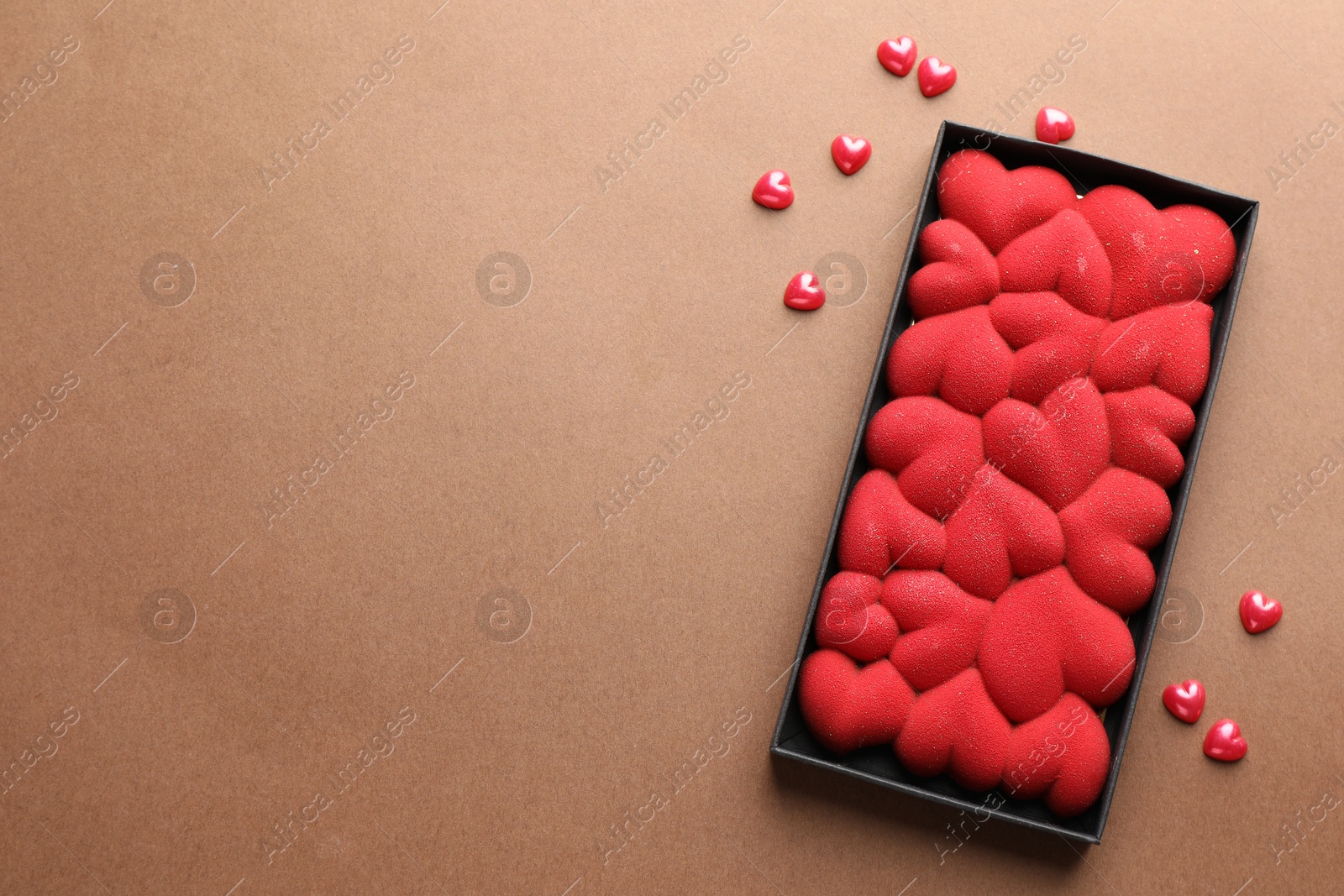 Photo of Chocolate bar decorated with hearts and confetti on brown background, top view. Space for text