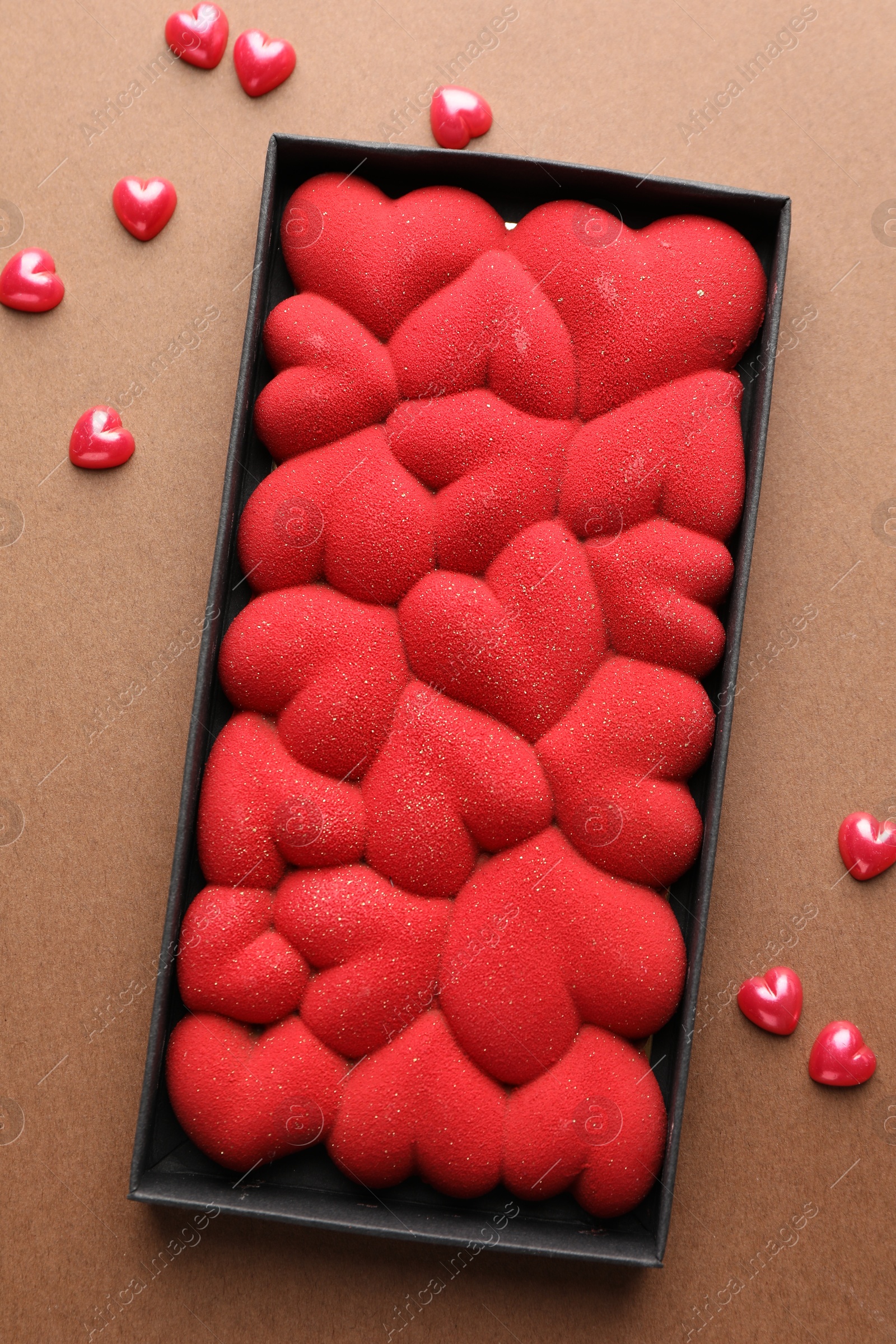 Photo of Chocolate bar decorated with hearts and confetti on brown background, top view