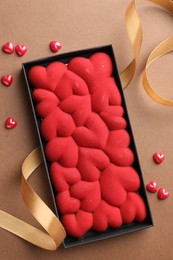 Photo of Chocolate bar decorated with hearts and confetti on brown background, top view