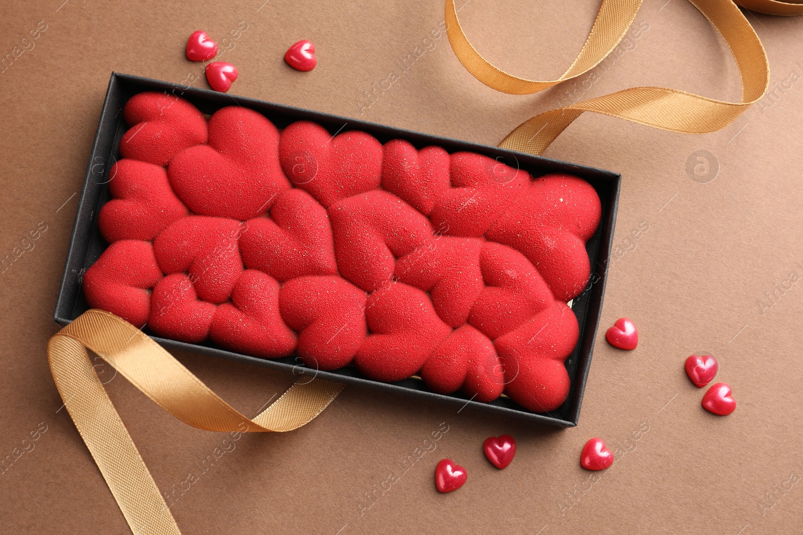 Photo of Chocolate bar decorated with hearts and confetti on brown background, top view