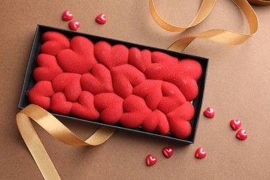 Photo of Chocolate bar decorated with hearts and confetti on brown background, top view