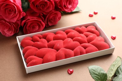 Photo of Chocolate bar decorated with hearts, confetti and roses on brown background, closeup