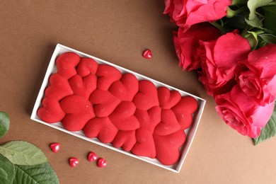 Photo of Chocolate bar decorated with hearts, confetti and roses on brown background, flat lay