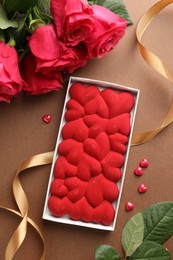 Photo of Chocolate bar decorated with hearts, confetti and roses on brown background, flat lay